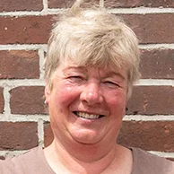 Die stolze Weiterbildungsteilnehmerin Astrid Estel steht, die Hände auf die Hüften gestützt, vor einer geziegelten Hauswand.